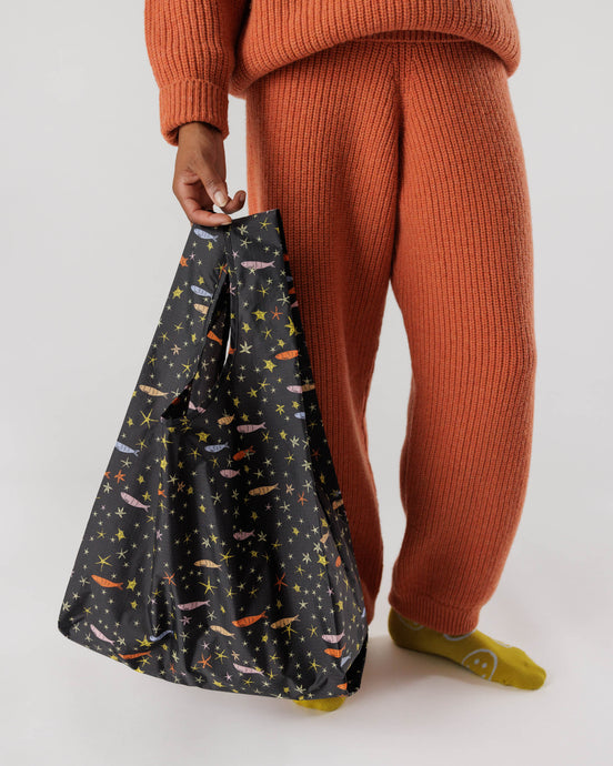 a person holding a baggu reusable shopping bag in a motif with stars and fish 