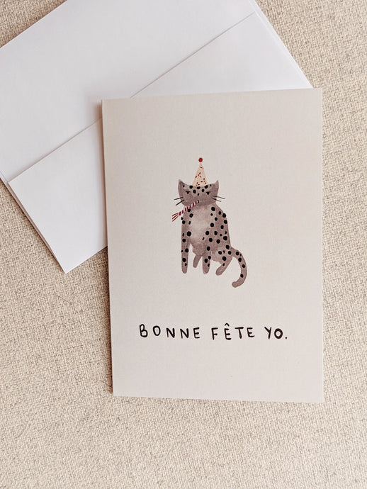 illustration of a cat with polka dots wearing a party hat and blowing a paper horn text bonne fete you