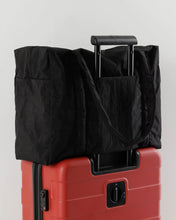 Load image into Gallery viewer, the black carryon tote cloud bag by baggu shown on a suitcase handle strapped on 
