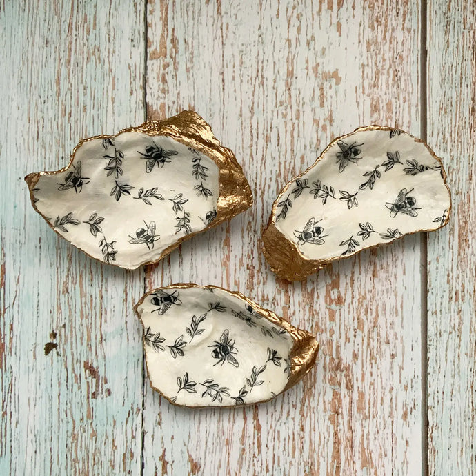a set of 3 oyster shells with small bees and herbs paited on the inside with a gold trim on edges 