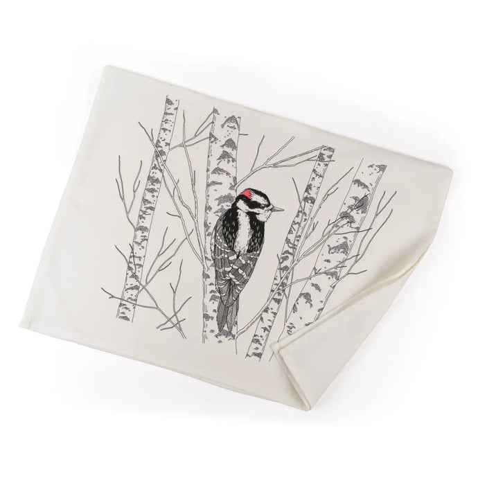 a white tea towel with a black drawing of a woodpecker bird in a birch tree 