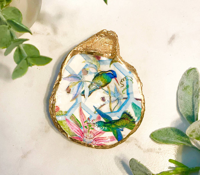 an oyster shell painted with hummingbirds and flowers and gold trim 