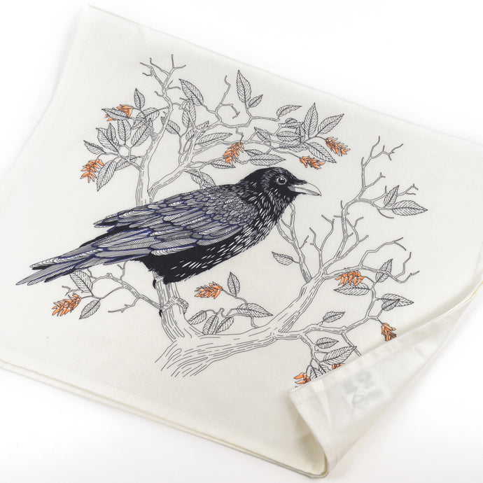a white tea towel whith an illustration of a black raven sitting on a tree branch 