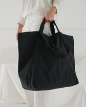 Load image into Gallery viewer, a person holding a large baggu black travel cloud bag 
