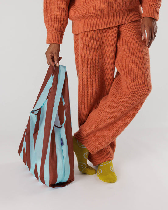 a person holding a baggu brand reusable shopping bag in a raisin awning stripe motif 