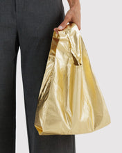 Load image into Gallery viewer, a person holding a metallic gold Baggu reusable bag 
