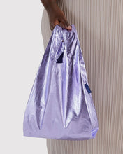 Load image into Gallery viewer, A person holds a metallic lavender reusable shopping bag with a small blue brand tag that reads 'baggu' against a light gray background and a pleated beige dress.
