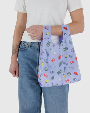 a peron holding a baggu brand reusable bag in a blue colour with small under the sea creatures 