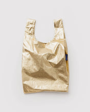 Load image into Gallery viewer, A metallic gold reusable shopping bag with a small blue tag on the side, that says baggu. photographed flat against a light gray background.

