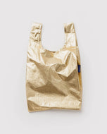 A metallic gold reusable shopping bag with a small blue tag on the side, that says baggu. photographed flat against a light gray background.