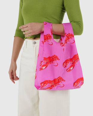 a person holding a baggu brand reuable bag in a hot pink colour with red lobsters on the fabric 