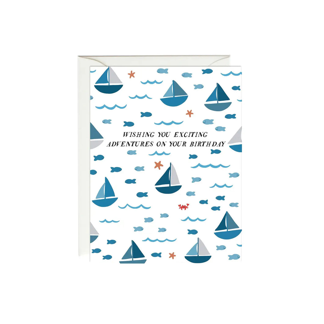 a white greeting card with blue sailboats and little fish illustrations, text. wishing you exciting adventures on your birthday 