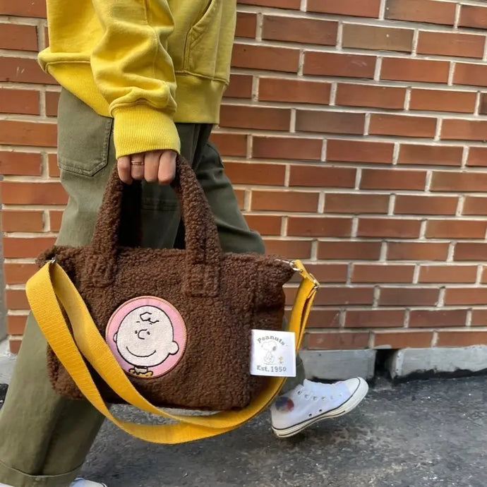 a person carrying a brown fuzzy tote bag with an emblem of charlie brown from the comics on it 