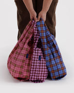 Plaid bags in pink, blue, and houndstooth pattern held by a person on a white background