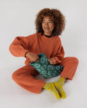 Load image into Gallery viewer, a person holding a baggu brand holiday stocking with happy faces on it. green in colour 
