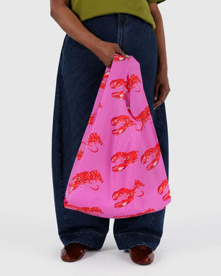 a person holding a hot pink coloured baggu reusable bag with red lobster motif 