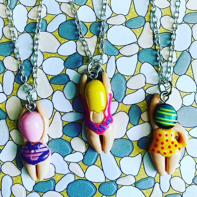 3 little swimmers in different bathing suits on necklace chains with a mosaic background 