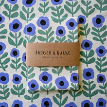 Load image into Gallery viewer, Folded tea towel with 'Badger &amp; Burke' branding on a floral patterned background
