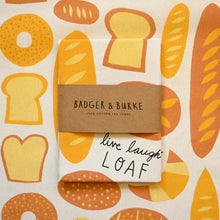 Load image into Gallery viewer, A folded cotton tea towel with a bread pattern, wrapped with a brown paper band reading 'BADGER &amp; BURKE 100% COTTON TEA TOWEL' and handwritten 'live laugh LOAF' on the front.
