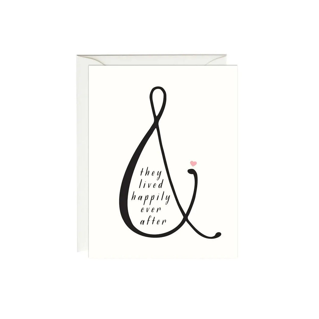 a white greeting card with large black ampersand and text they lived happily ever after, with a small pink heart 