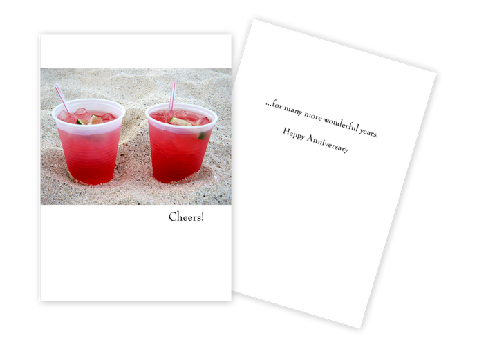 colour photo of two cocktail glasses on a beach on a white greeting card. text cheers 