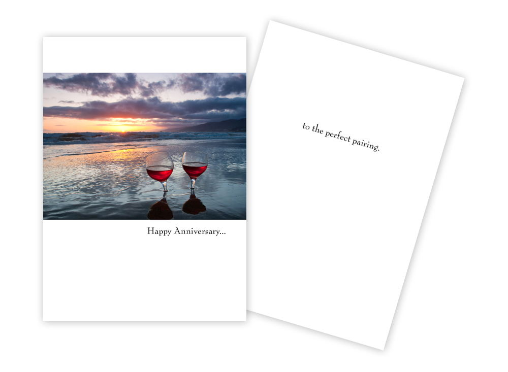 colour phot of two glasses of wine on a sunset beach on a white greeting card