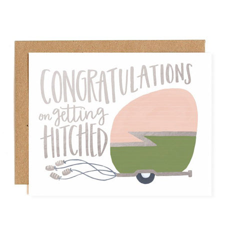 an illustration of a pink and green camper trailer with cans on strings attached on the bottom on white background in silver script congratulations on getting hitched with kraft envelope 