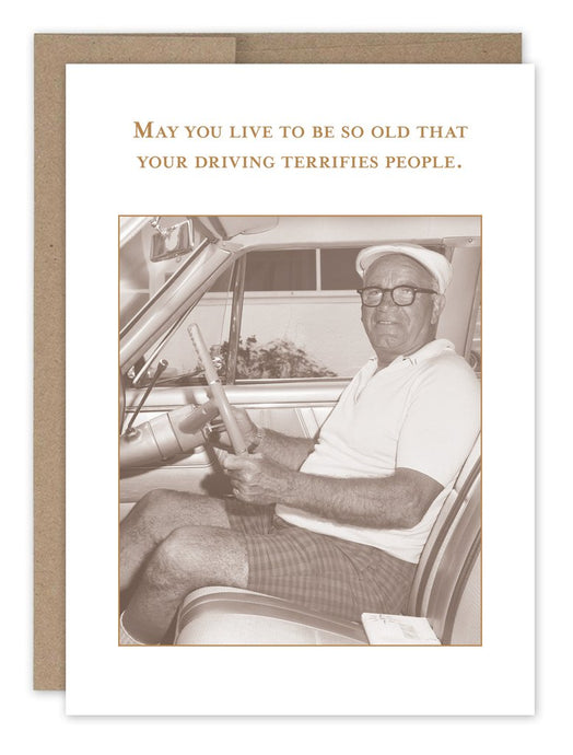 a sepia tone photo of an elderly man at the wheel of a car . he has on shorts, a gold shirt, and hat. smiling at the camera in an older vehicle 