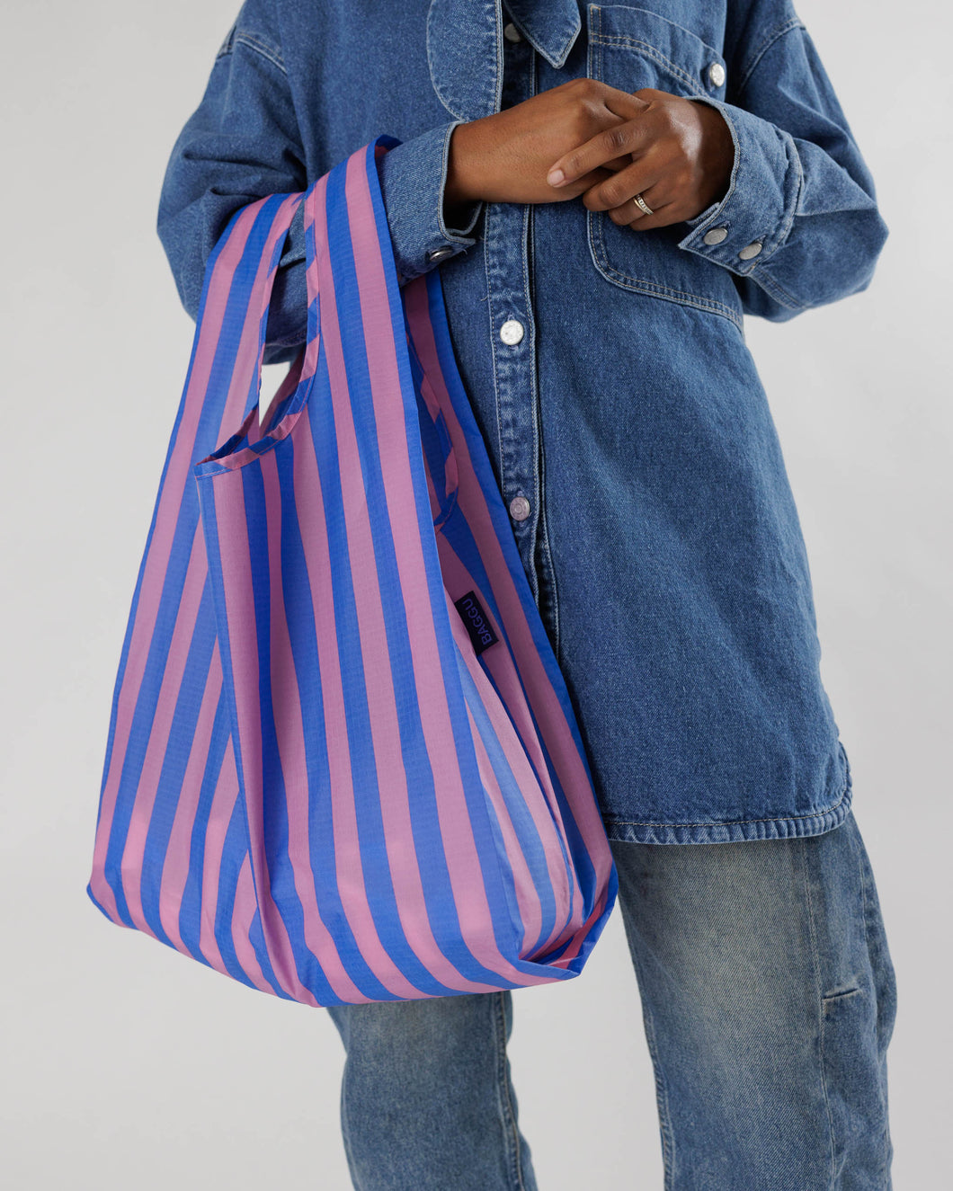 a person holding a baggu reusable shopping tote with a blu and pink awning stripe as the pattern 