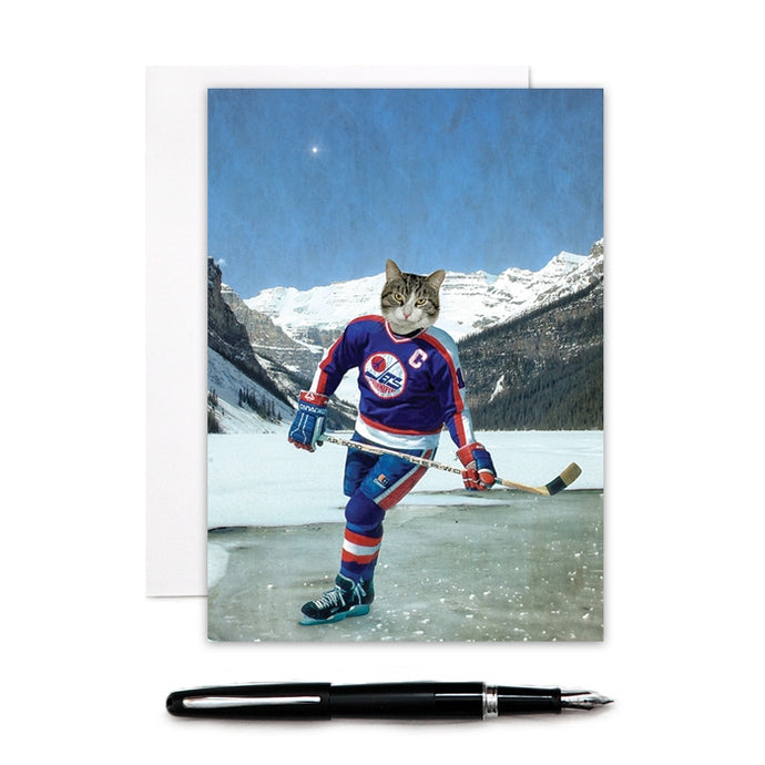a colur phot of a grey tabby cat wearing a Winnipeg jets uniform playing hockey on ice in front of large mountains like lake louise canada 