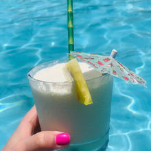 画像をギャラリービューアに読み込む, a photo of a cocktail with a piece of friut a bamboo straw and a tiny cocktail umbrella on it. with blue pool water in the backdrop

