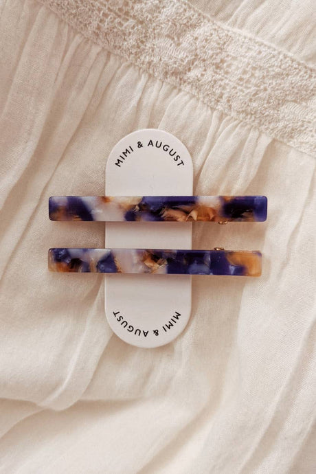 two narrow hair clips in a tortoise colouring  style with pearl, blue and brown marbling on a tag that says mimi and august 