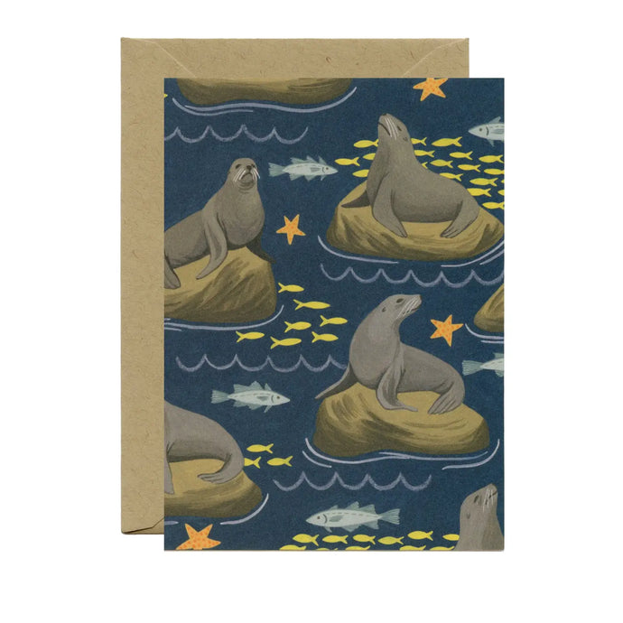 a greeting card with illustration of several seals sitting atop of rocks iin the water with small schools of fish swimming by. no text