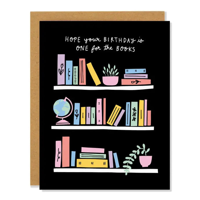 a greeting card by badger and burke with an illustration of a colourful bookcase with books and plants and objects , text hope your birthday is one for the books