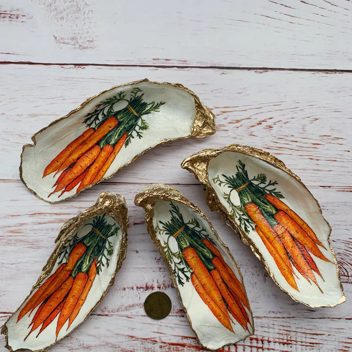 A collection of four oyster shells with painting inside of bunches of carrots with gold edges on the trim
