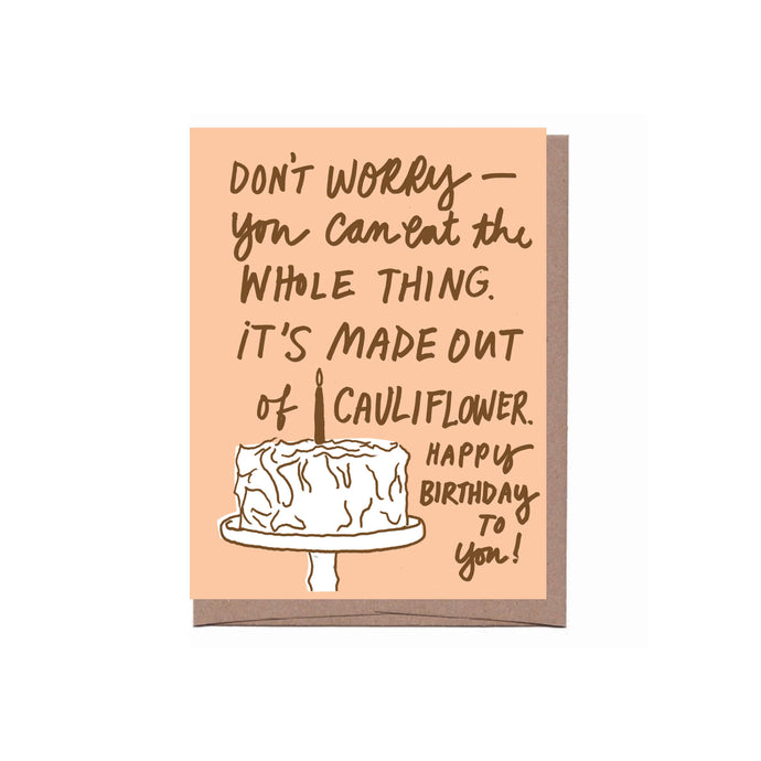 a beige card with wrting on it. don't worry you can eat ithe whole thing it is made out of cauliflower happy birthday to you with a white cake and one candle on a cake stand with a brown kraft envelope 