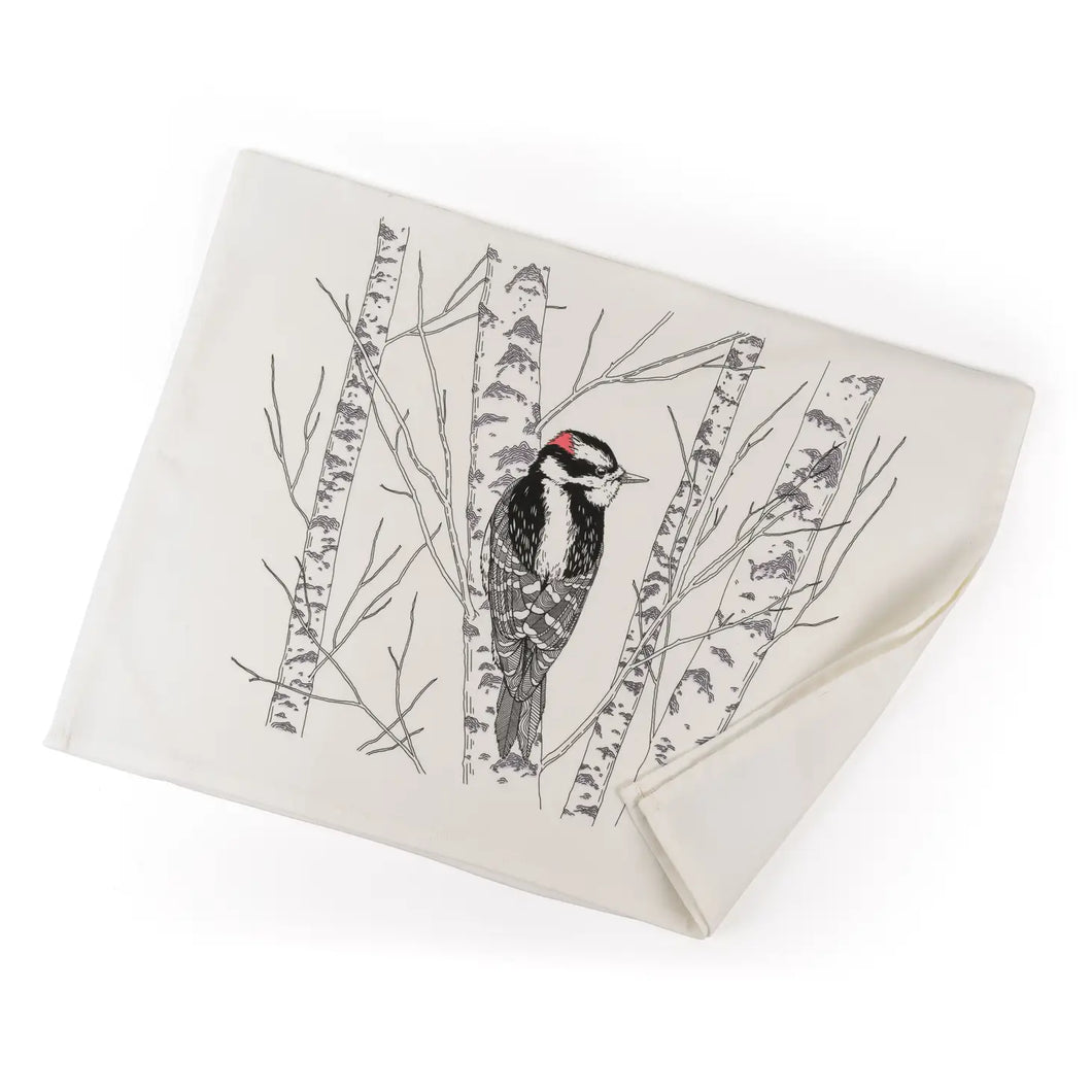 a white tea towel with a black drawing of a woodpecker bird in a birch tree 