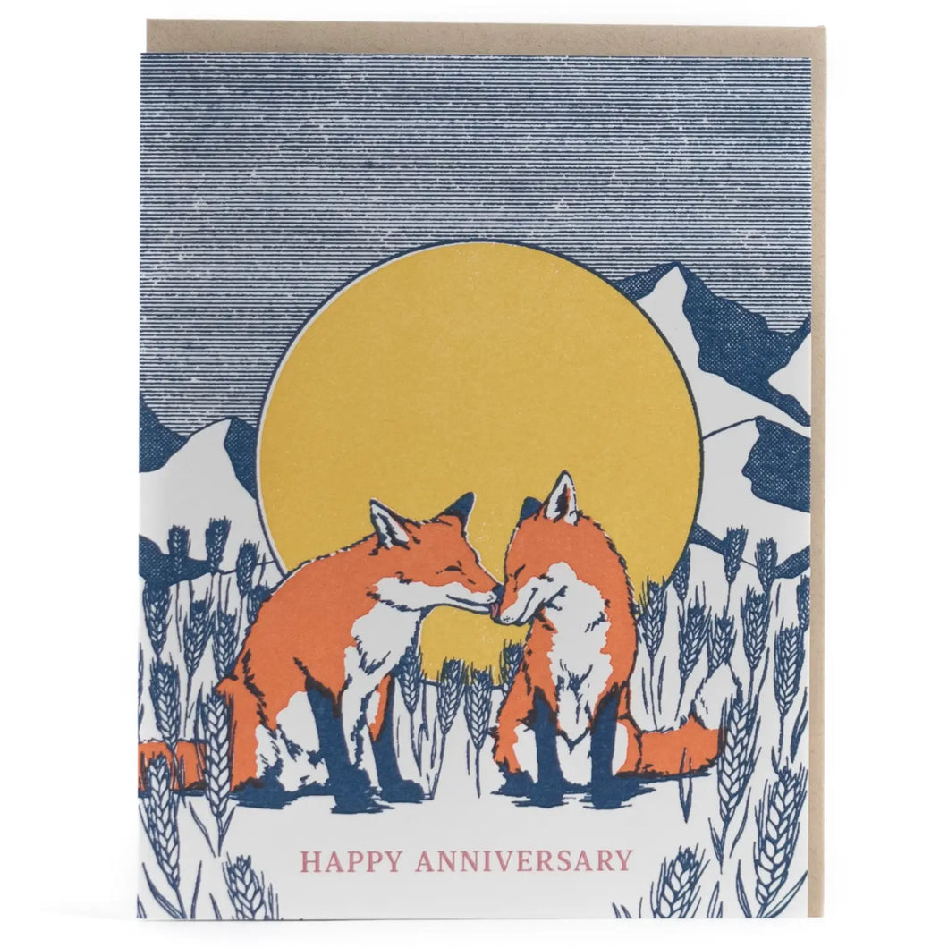 colour illustation of a greeting card with two red foxes nuzzling in front of a large moon and mountain scape with text happy anniversary 