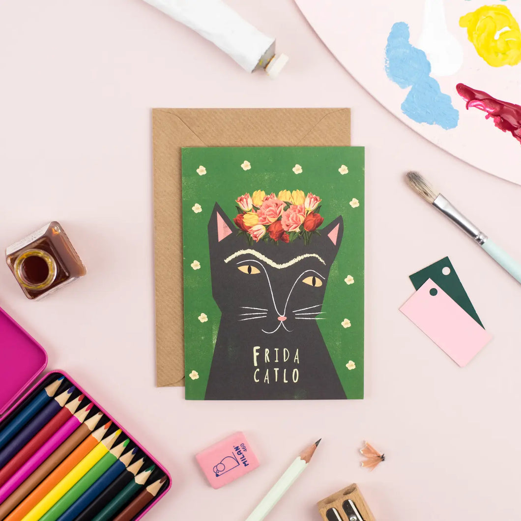 A greeting card with image of a black cat that mirrors the look of frida khalo the mexican artist. with long eyebrow and flowers on top of its head 