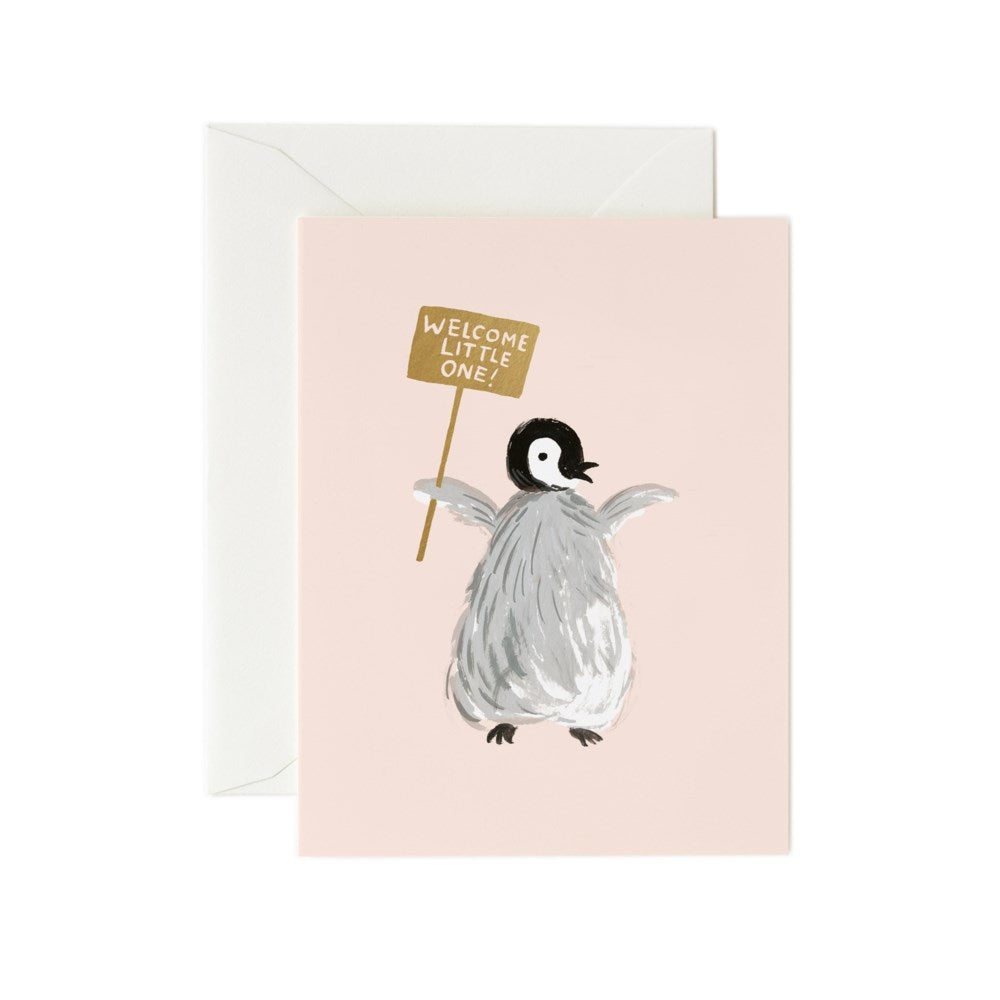 a greeting card with a soft peach pink backround and an illustration of a penguin holding a little sign with text welcome little one 