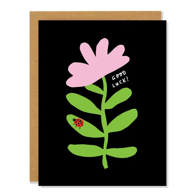 a black greeting card with a mauve flower and green stem, very modern, little red ladybug on stem. text good luck