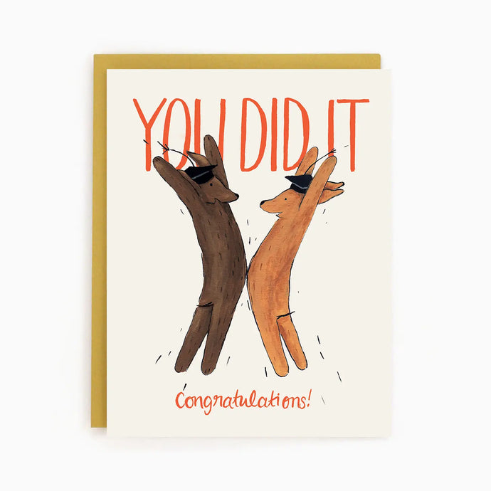 a greeting card with an illustration of 2 dogs standing tall and high fiving each other, wearing mortarboards on the head text you did it congratulations 