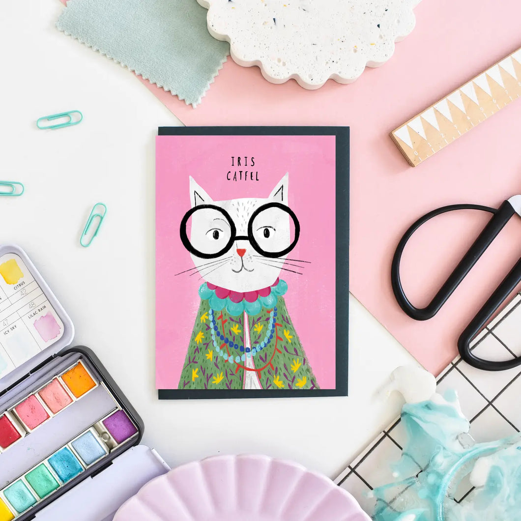 A greeting card with image of a white cat wearing big black glasses and looks like famous iris Apfel. text Iris Catfel