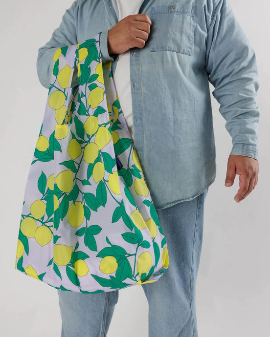 a person holding an open big baggu shopping bag with lemon tree motif on pale blue fabric 
