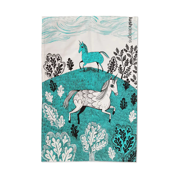 a tea towel with two unicorns that appear to be galloping across a meadow 