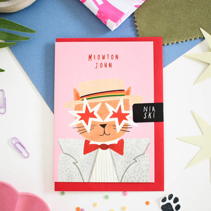 a greeting card depicting an image of music legend elton john as a cat, wearing a hat and big star shaped sunglasses. text meowton john