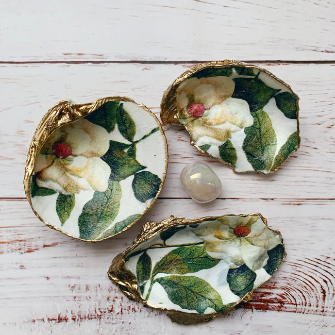 a set of three oyster shells with magnolia flowers painted n inside and gold trim around the shells 
