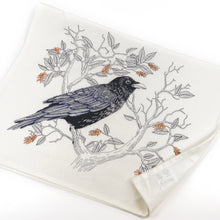 Load image into Gallery viewer, a white tea towel whith an illustration of a black raven sitting on a tree branch 
