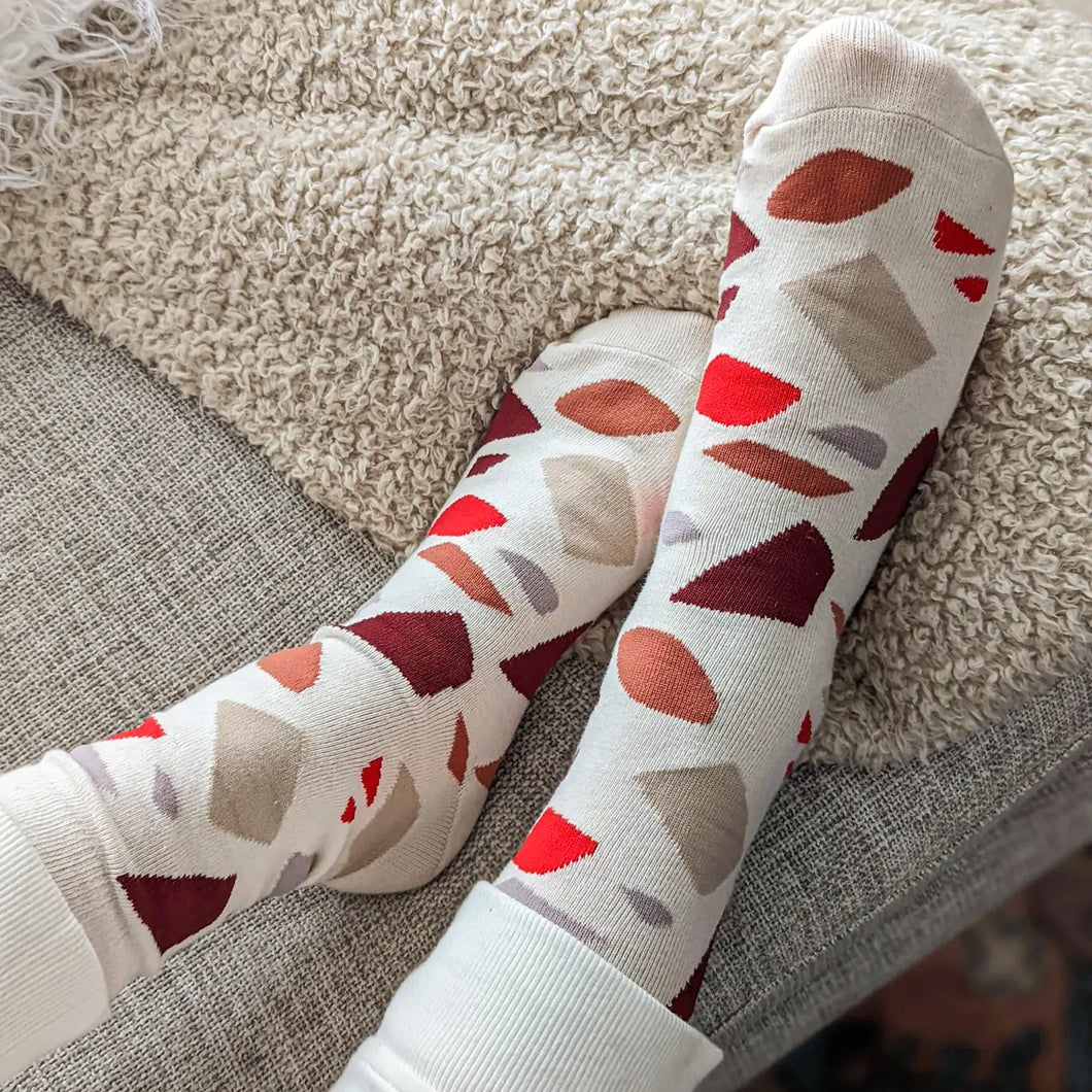 photo of a pair of socks being worn by a person. shapes of terrazzo in reds and greys and browns 