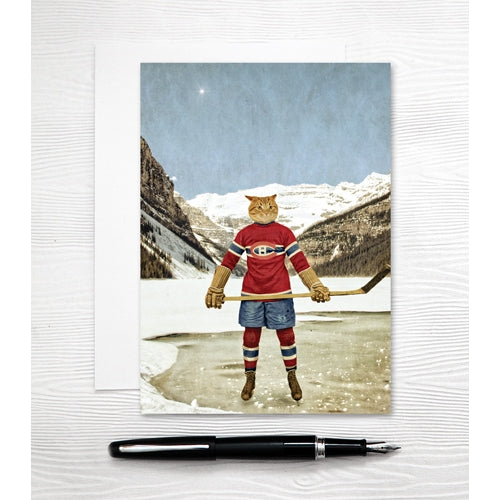 a colour phot of an orange tabby cat wearing a Montreal Canadians hockey uniform holding a stick and weraing skates on a frozen lake in front of a large mountain range 